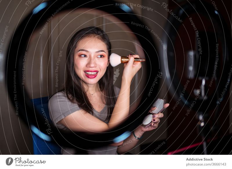 Beauty blogger applying makeup during shooting session beauty vlog woman cosmetic foundation record video young asian female ethnic camera light lamp mirror