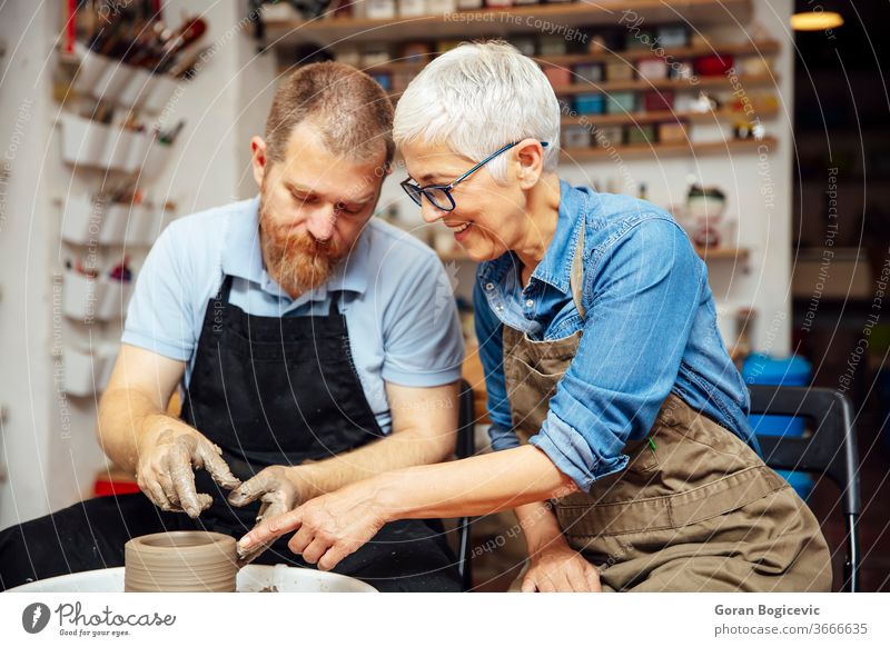 Senior woman spinning clay on a wheel with teacher at pottery class lady instruction instructor learn shape finger turn ceramic skillful artist shaping hand