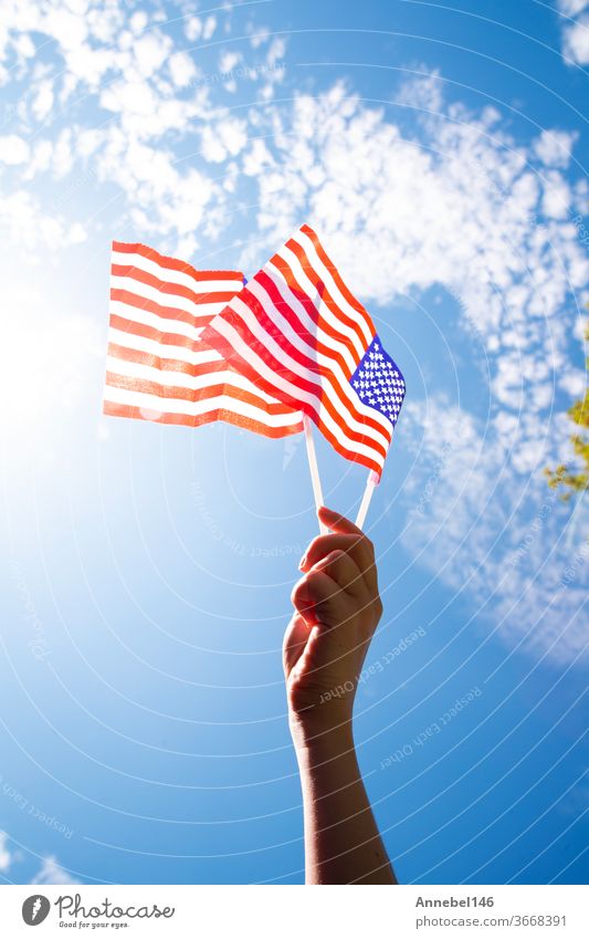 Hand holding two american flags on the blue sky with sunlight background, waving flag for United States of America close-up national patriotism red freedom usa