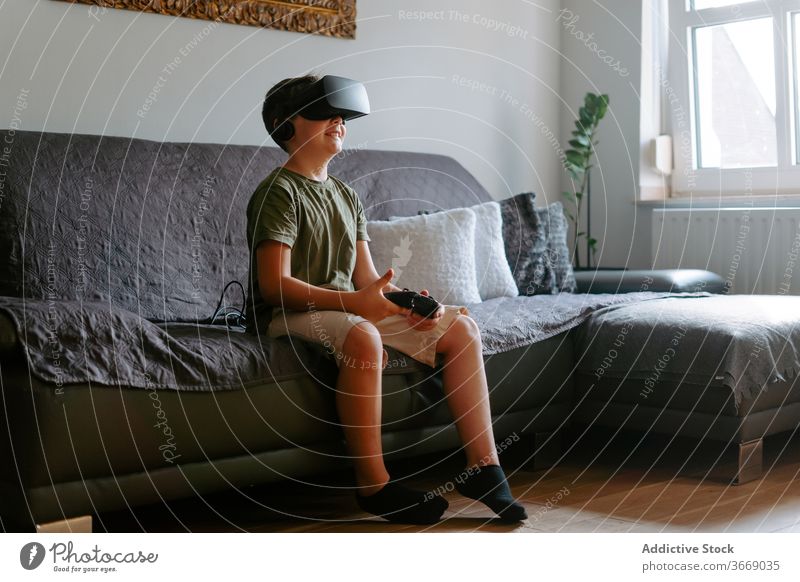 Child in VR headset playing on couch boy vr goggles gamepad virtual reality using sofa entertain modern home device child kid little adorable gadget childhood