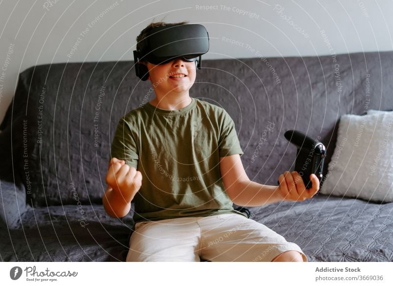 Child in VR headset playing on couch boy vr goggles gamepad virtual reality using sofa entertain modern home device child kid little adorable gadget childhood