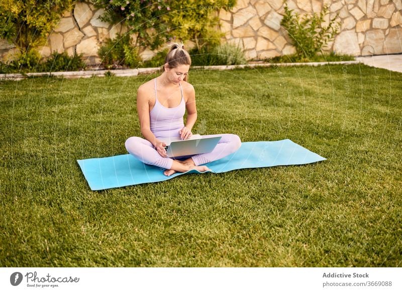 Tranquil woman using laptop on mat in courtyard online tutorial yoga choose pick tranquil sportswear female barefoot calm wellness healthy slim gadget device