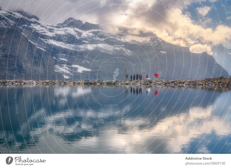 Group of tourists admiring lake near snowy ridge in evening reflection cloud tourism breathtaking paradise picturesque highland majestic river travel idyllic