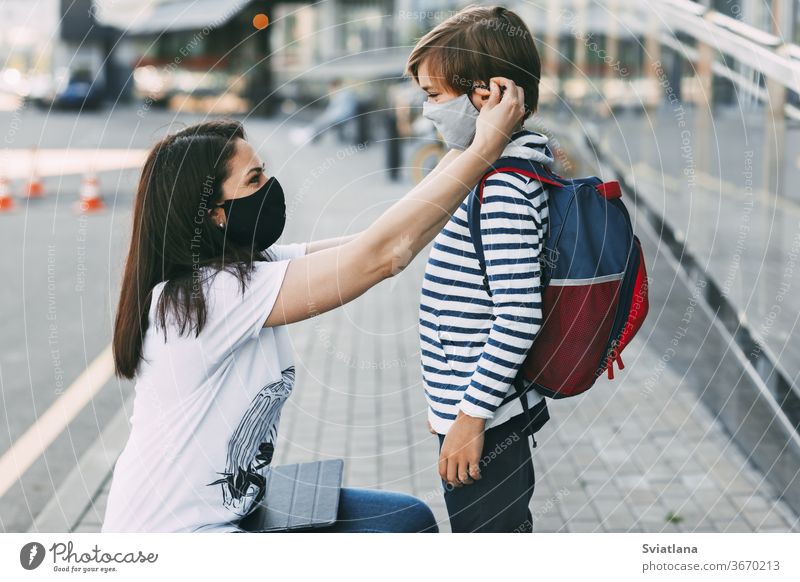 Mother adjusts her son's mask. A mother and child on their way to school or kindergarten during a coronavirus pandemic. Protective mask as a disease prevention, social distance