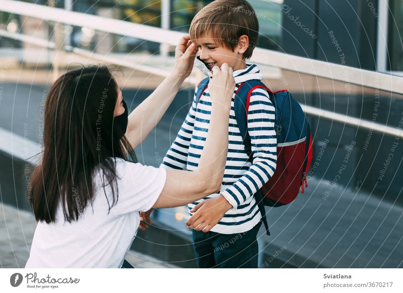 Mother adjusts her son's mask. A mother and child on their way to school or kindergarten during a coronavirus pandemic. Protective mask as a disease prevention, social distance