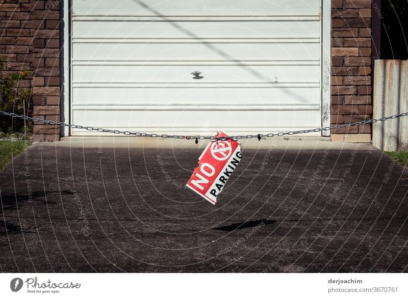 "NO P A R K I N G" is located on a garage entrance on a chain. no parking Parking lot Signs and labeling Street Traffic infrastructure Lanes & trails Deserted