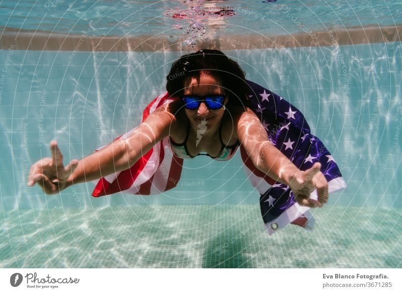 young woman in a pool holding american flag underwater. 4th july independence day concept. Summertime swimming pool summer sunglasses caucasian fun beautiful