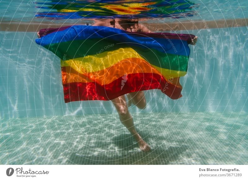 young woman in a pool holding rainbow gay flag underwater.LGBTQ concept. Summertime swimming pool love hugs lesbian homosexual equality attractive people female