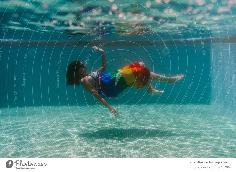 young woman in a pool holding rainbow gay flag underwater.LGBTQ concept. Summertime swimming pool love hugs lesbian homosexual equality attractive people female