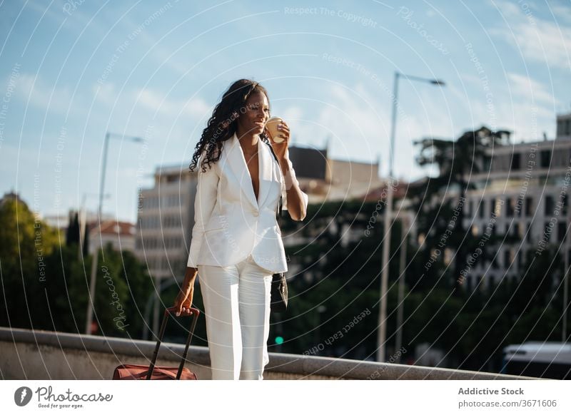 Elegant ethnic businesswoman walking in downtown with cup of coffee baggage street trip style city cheerful tourist architecture vacation travel weekend female