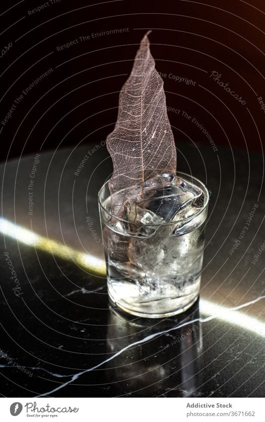 Alcohol drink with decorative leaf cocktail alcohol ice bar table cold cube beverage refreshment cup glass party booze transparent portion serve crystal chill