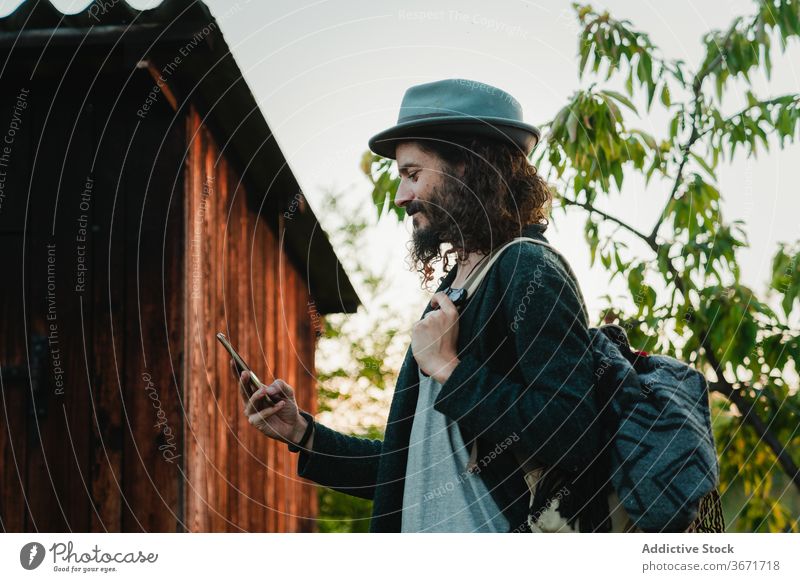 Traveling man using smartphone in countryside hipster browsing travel rural nature tourism male mobile surfing style beard trendy backpack smile content guy