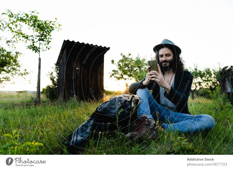 Relaxed man browsing smartphone on meadow hipster social media chat field summer relax using male nature weekend green happy cheerful internet rest connection