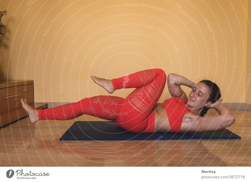 Pretty woman with sportswear having a good time exercising in the living room of her house due to the coronavirus. Brunette fit European girl working her abs. Healthy life style.