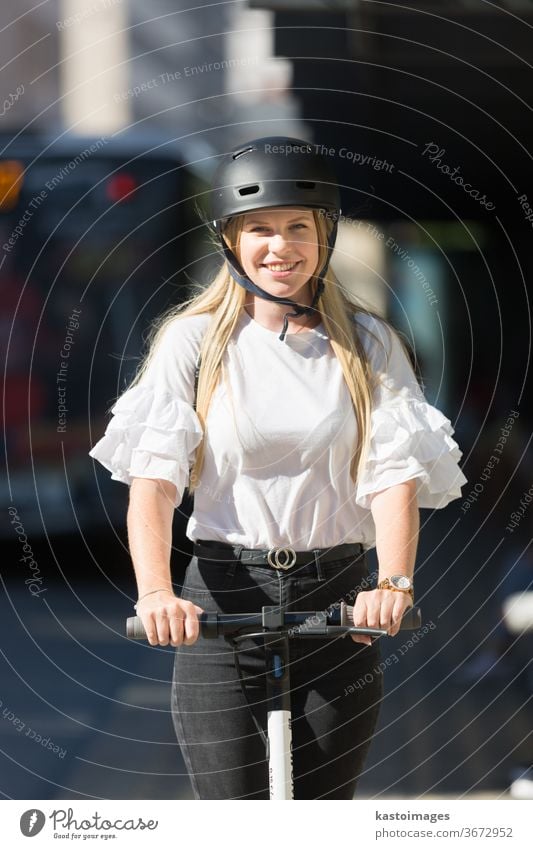 Trendy fashinable teenager, beautiful blonde girl riding public rental electric scooter in urban city environment. Eco-friendly modern public city transport