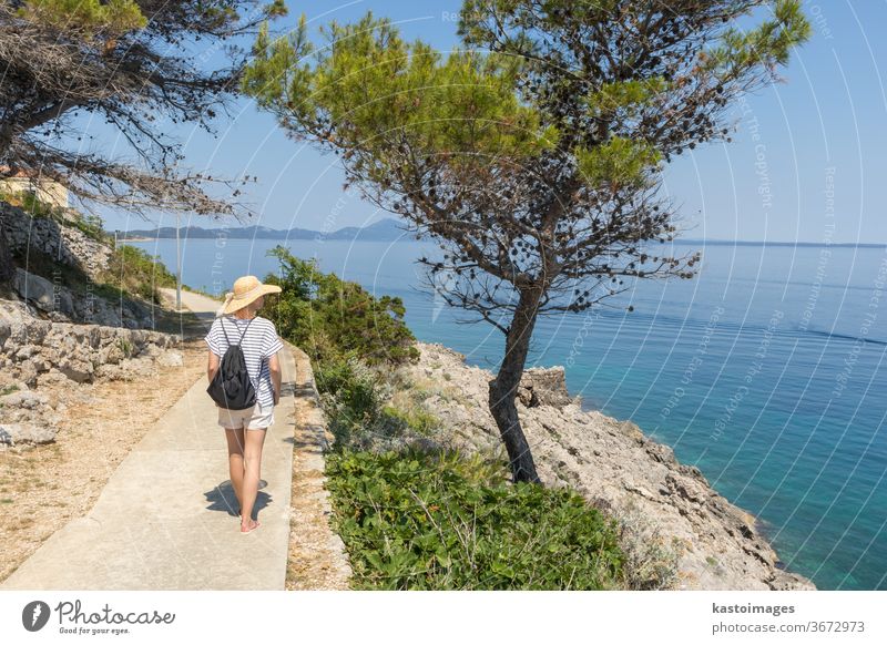 Young active feamle tourist wearing small backpack walking on coastal path among pine trees looking for remote cove to swim alone in peace on seaside in Croatia. Travel and adventure concept.