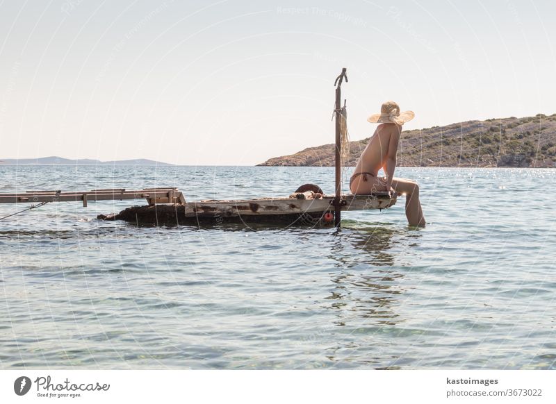 View of unrecognizable woman wearing big summer sun hat tanning topless and relaxing on old wooden pier in remote calm cove of Adriatic sea, Croatia. leisure