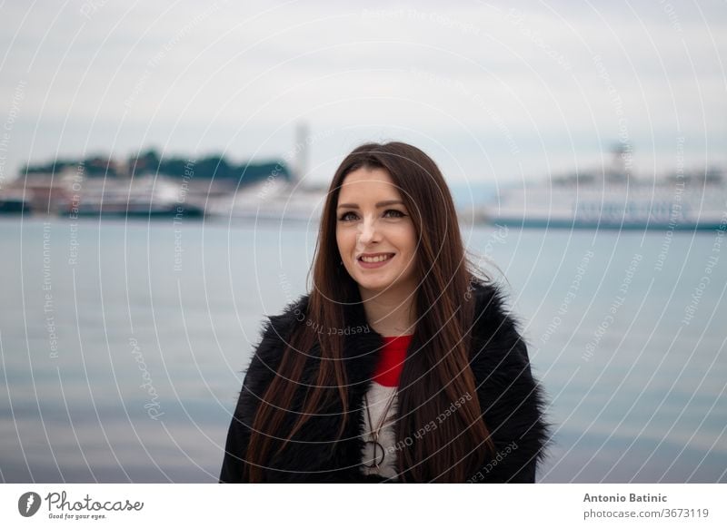 Attractive brunette in a black furry coat posing on a summer day with blue adriatic sea and ferries in the distance. Town of Split, Croatia attractive autumn