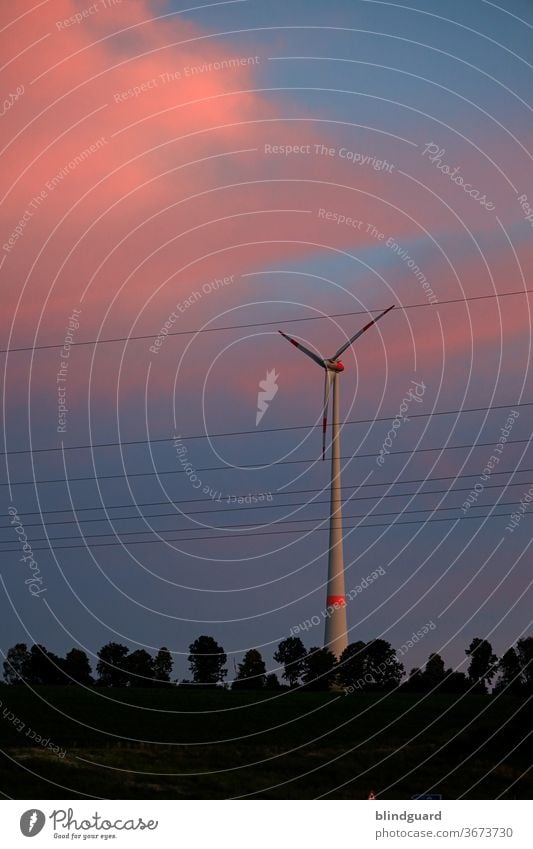 Energy in the sunset. Wind power behind power lines and trees, in front of orange-red evening clouds. Energy industry Wind energy plant wind power Weather