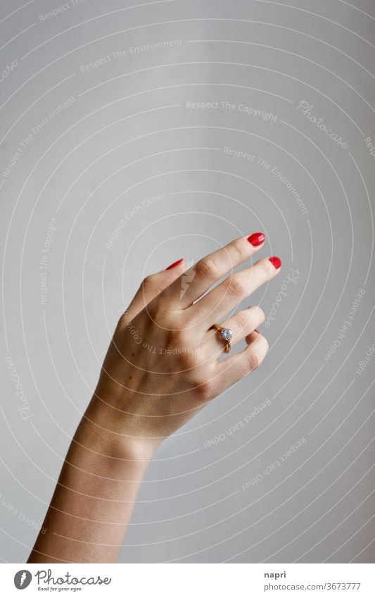 graceful | Right hand of a young woman with a brilliant ring on her ring finger and red painted fingernails in front of a neutral background. by hand