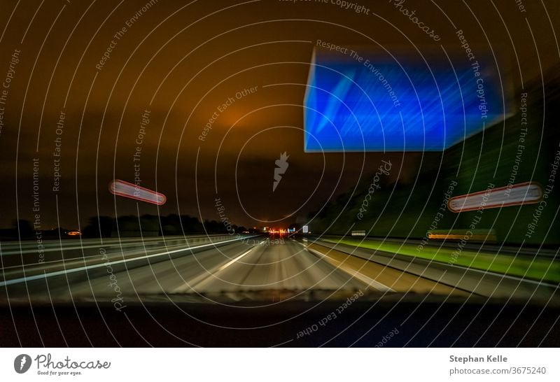 The long exposure shot of a highway during the night while driving fast over a german Autobahn and a typical blue sign. light building background autobahn