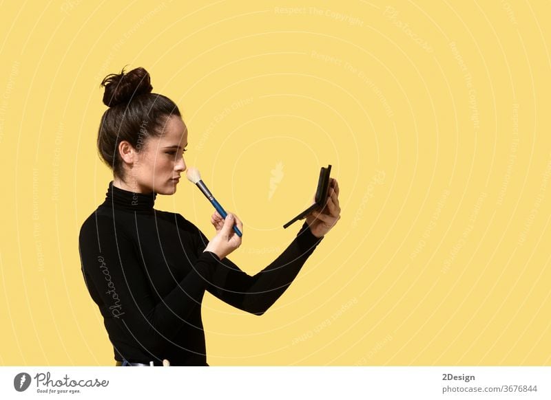 Side view of a young woman with ponytail using the phone as a mirror while applying makeup brush on face skin sitting outdoor day make-up adult one person