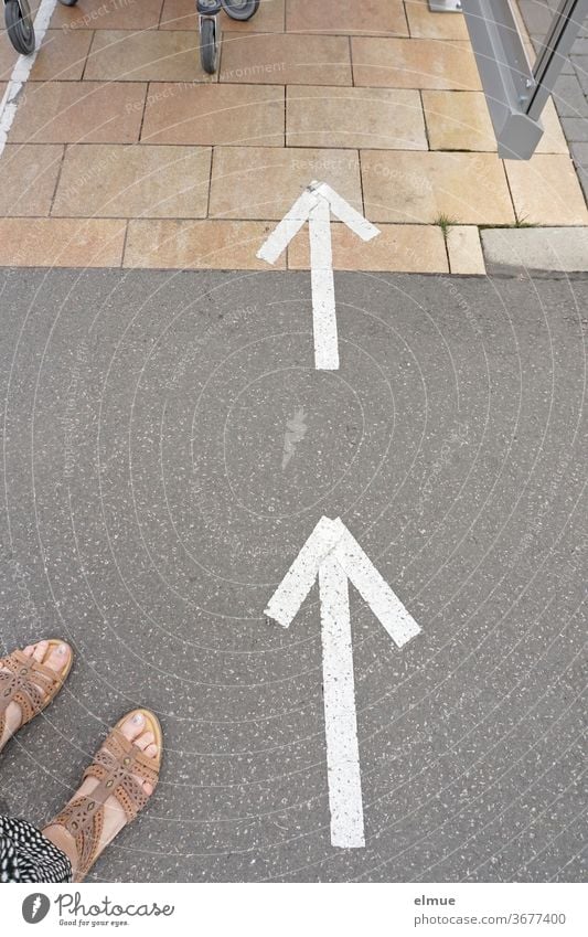 two care panels on the floor indicate shopping trolleys, two feet in sandals are visible on the edge Arrow Shopping Regulation direction of arrow everyday life