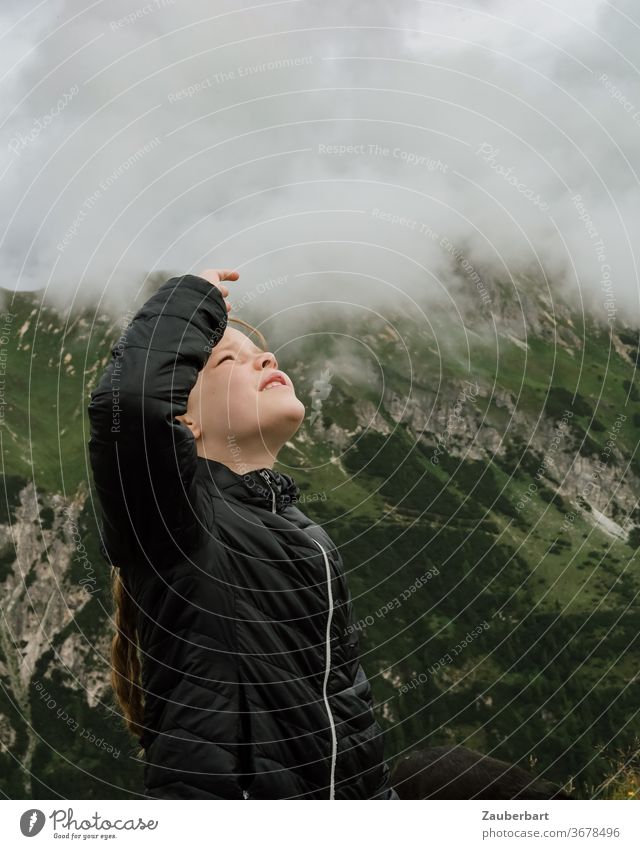 Little girl looks at the clouds in the Alps in South Tyrol Child Observe Clouds Quilted jacket Small Black mountains green Hiking by hand Profile Looking wide