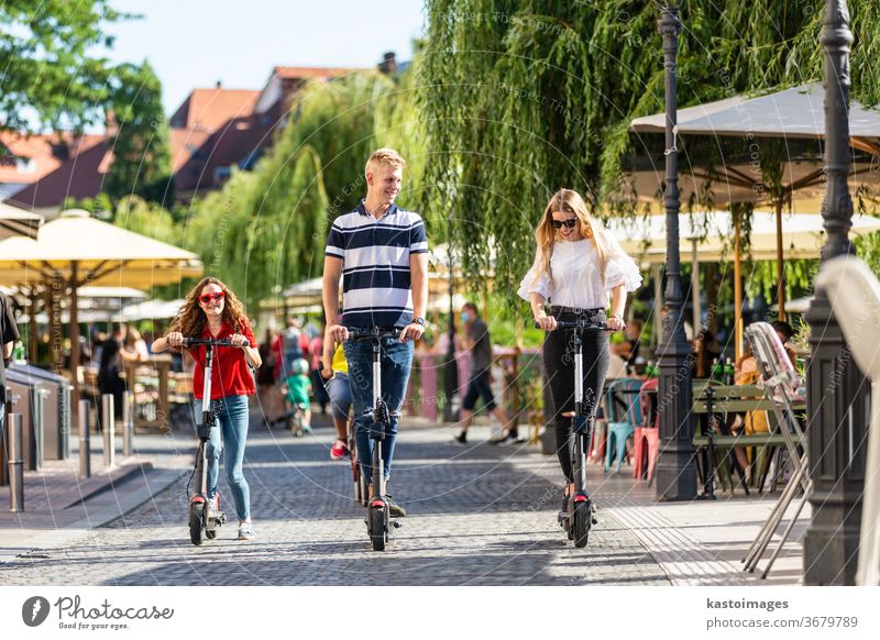 Trendy fashinable group of friends riding public rental electric scooters in urban city environment. New eco-friendly modern public city transport in Ljubljana, Slovenia