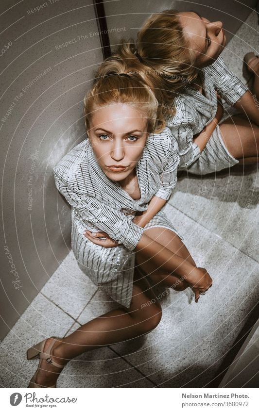 Beautiful blonde model sitting in the corner. She has a serious expression and is wearing a stylish white dress. High view. luxury fashion caucasian portrait