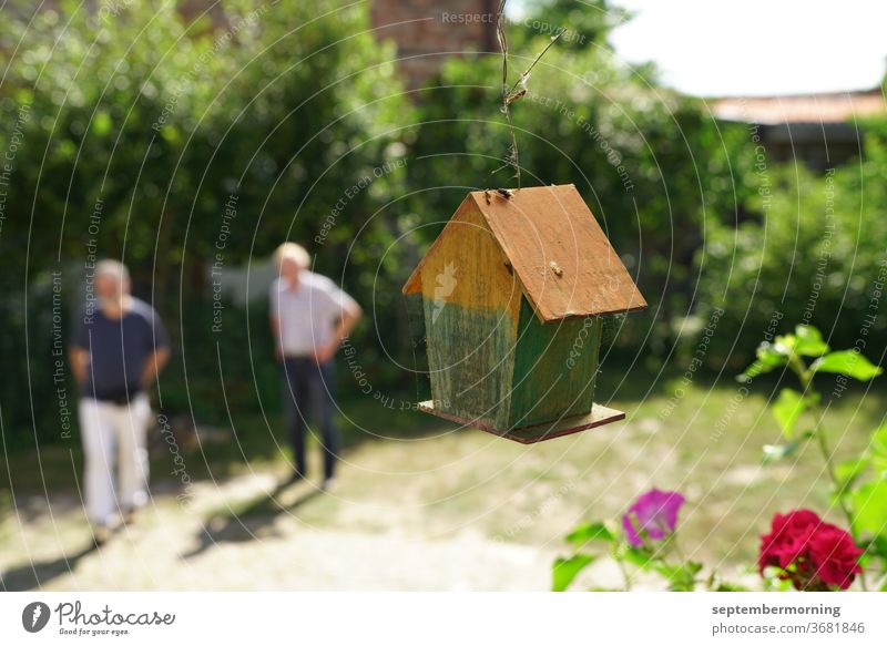 Bird house from behind, hanging Bird house made of wood 2 men unsharp in the background Summer in the garden red flower in the foreground Pastel shades