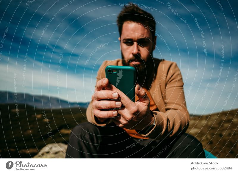 Bearded hiker using smartphone in mountains man countryside sky cloudy rest puerto de la morcuera spain male travel journey mobile relax internet nature trip