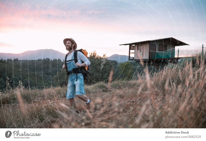 Happy man in rural area traveler sunset mountain enjoy field backpack tourist evening male picturesque sundown smile wanderlust sky tourism village happy