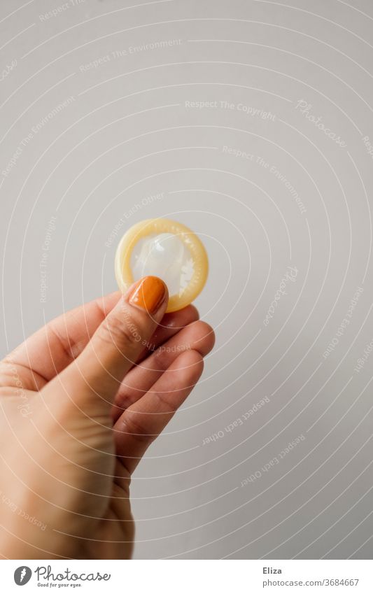 A female hand holds a condom against a neutral background. Topic Contraception. prevention Condom feminine woman's business go along with by hand Protection