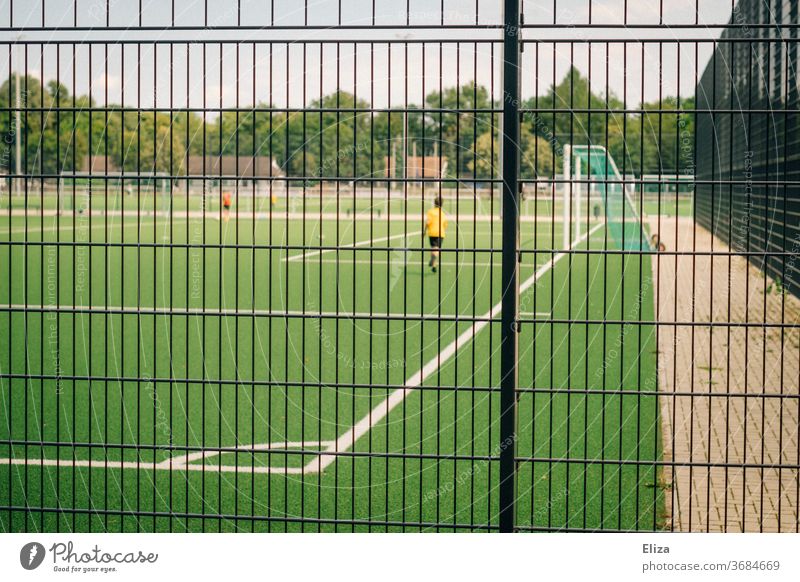 Young footballer on a football field behind a fence soccer soccer field Football pitch Sports Playing Sporting grounds Fence Ball sports Leisure and hobbies