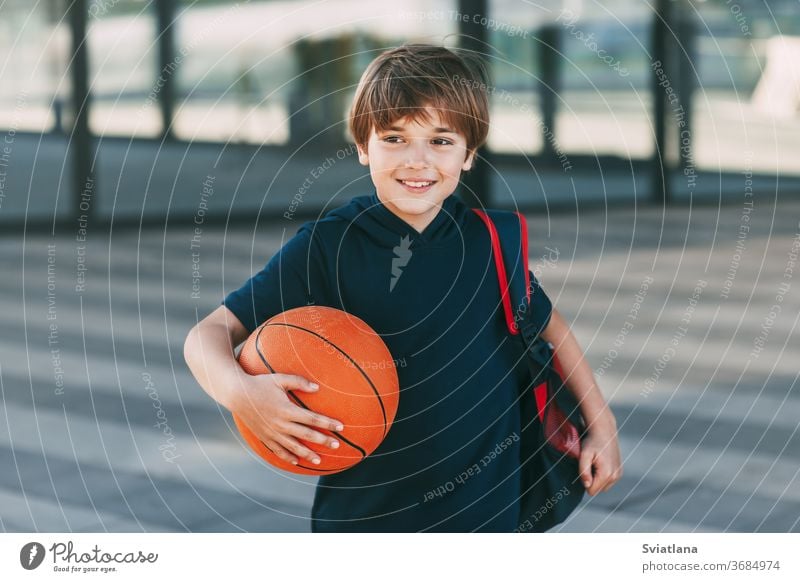 Portrait of a beautiful boy in sports uniform with a backpack and a basketball. The boy smiles and holds the ball in his hands. Training, education, physical education