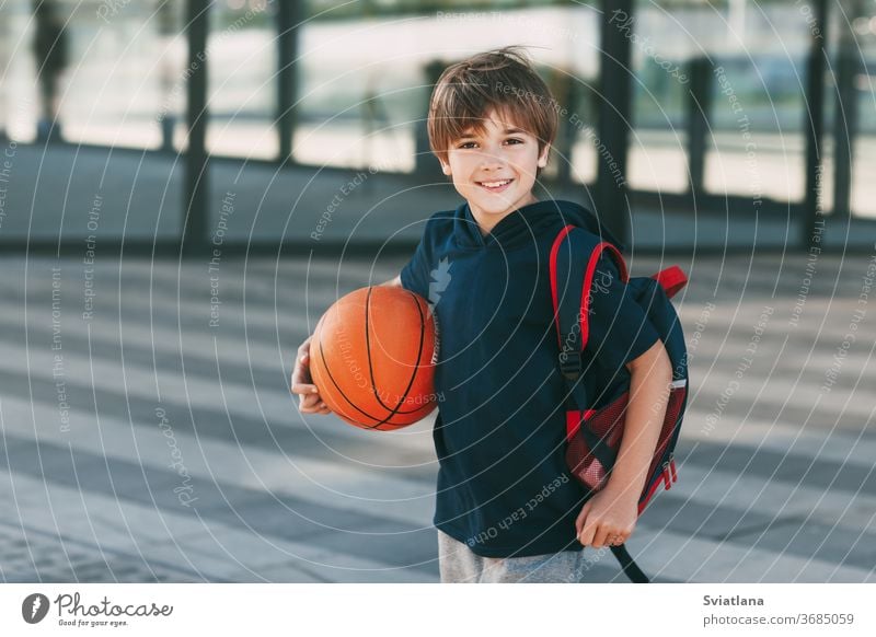 Portrait of a beautiful boy in sports uniform with a backpack and a basketball. The boy smiles and holds the ball in his hands. Training, education, physical education