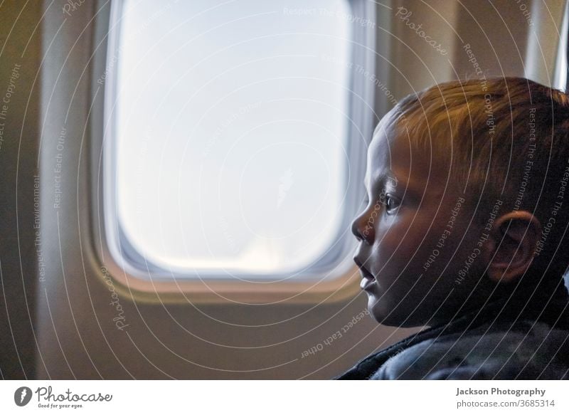 Serious toddler sitting next to the window in the airplane kid serious travel boy copy space uncertain scared curious small caucasian face view indoor concept