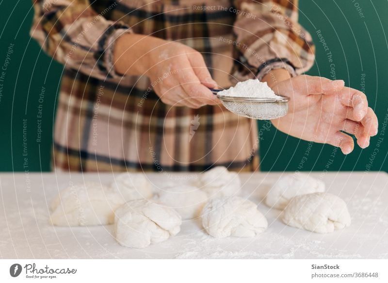 Woman sprinkles flour to handmade pieces of dough for bread, homemade cooking. woman hands white person powder pasta working bake-house food pizza female pastry