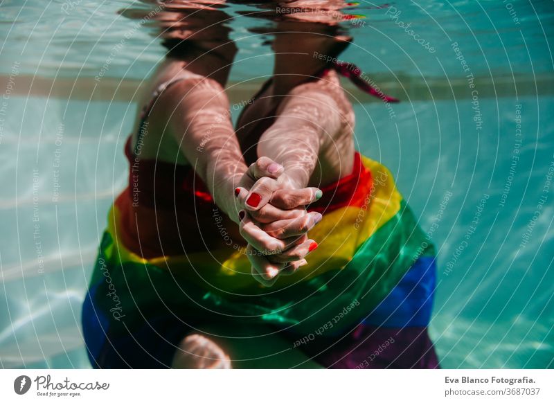 two women at the pool together wrapped with rainbow gay flag. LGBT concept love lesbian underwater swimming pool floating summer lgbt dating romantic bisexual