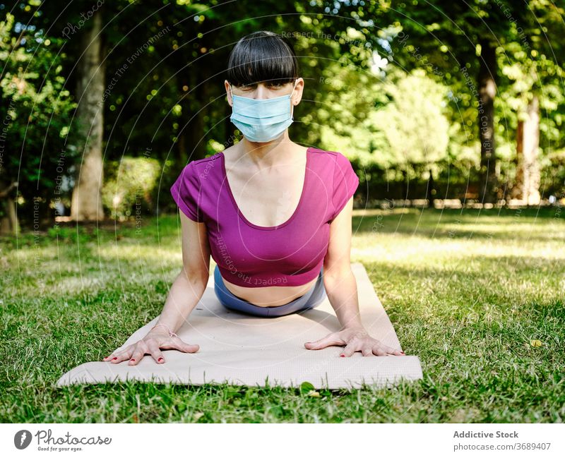 Woman doing yoga in Cobra pose in park woman cobra pose mask coronavirus female tranquil flexible relax green harmony outbreak summer wellness nature serene