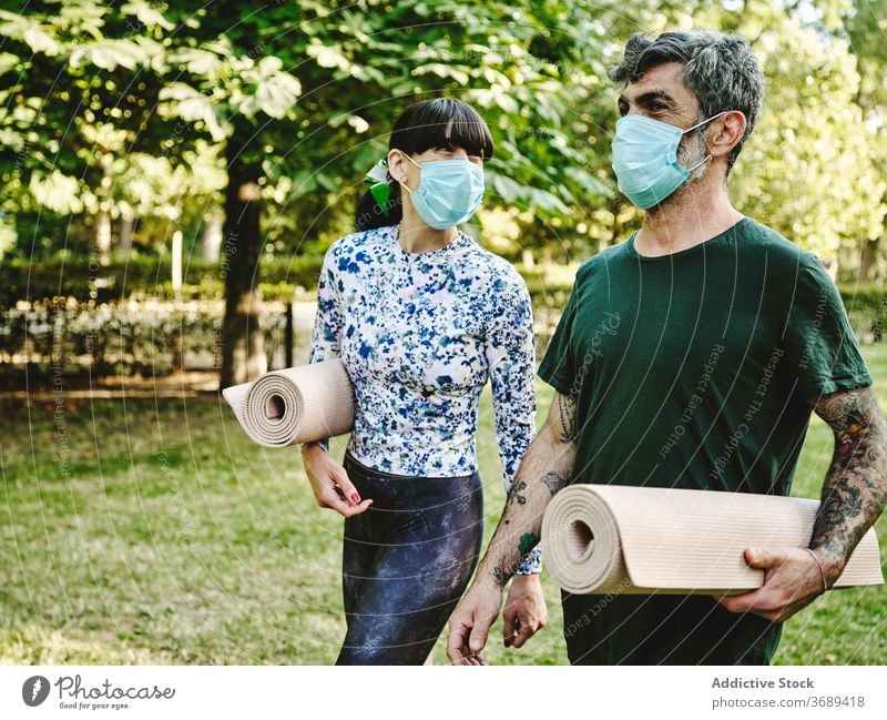 Cheerful couple with medical masks and yoga mats walking in park cheerful together coronavirus covid pandemic covid19 new normal infection positive talk happy