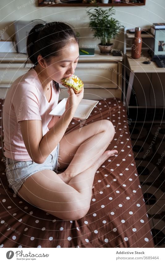 Ethnic woman eating breakfast on bed toast avocado egg delicious healthy nutrition morning female ethnic asian cozy home food relax comfort tasty meal fresh