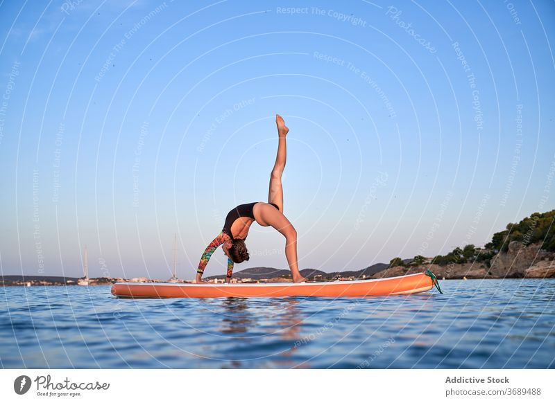 Flexible woman doing yoga on paddleboard sunset pose surfer balance sea female water healthy nature harmony relax tranquil serene sky calm ocean peaceful lady