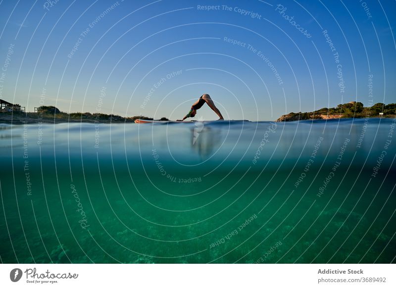 Flexible woman doing yoga on paddleboard sunset pose surfer Adho Mukha Svanasana balance sea female water healthy nature harmony relax tranquil serene sky calm