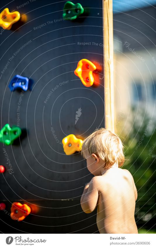 Child standing in front of a climbing wall Playing Climbing Infancy Climbing wall Playground Summery ardor Boy (child) anxiously timid cautious