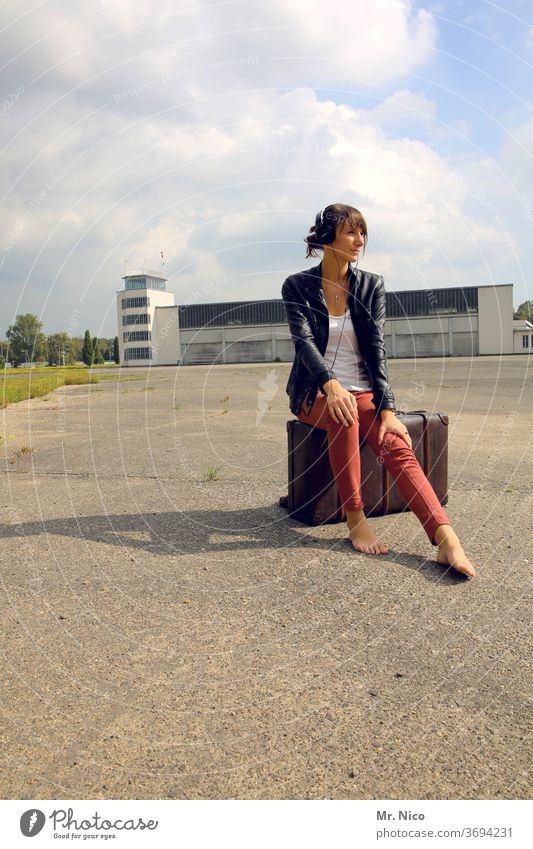 Young woman sits on her suitcase and waits on the tarmac for the plane to go on holiday Summer Vacation & Travel Sit Wait Airport Lifestyle Listening Barefoot