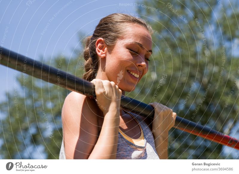 Young  brunette woman doing pull-up on a sports horizontal bar at summer day workout outdoor training people exercise fitness body strong young person adult gym