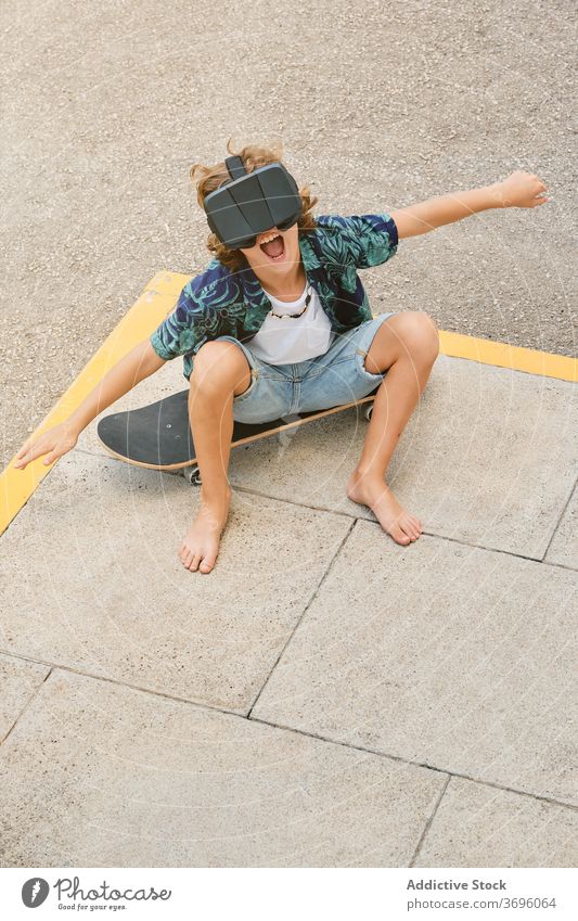 Boy sitting on a skateboard wearing virtual reality glasses and gesturing as he flies vertical reaction touching optical dimensional experience headset