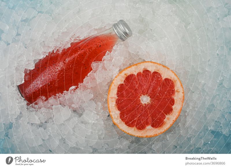 Bottle of red grapefruit drink on ice Cocktail pink juice soda chia seeds basil alcohol bottle glass transparent clear one cold crushed half cut slice closeup